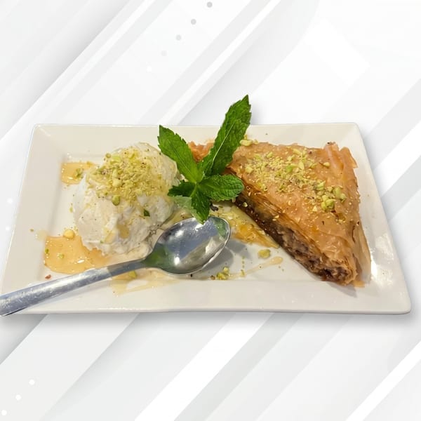 A slice of baklava with a scoop of vanilla ice cream, drizzled with honey and pistachios.