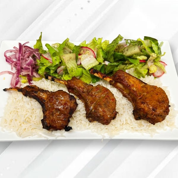 Three grilled lamb chops on a bed of white rice, with a side of green salad and red onions.