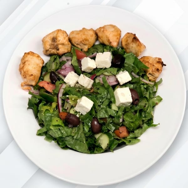 A fresh green salad with feta cheese, olives, and grilled chicken pieces on a white plate.