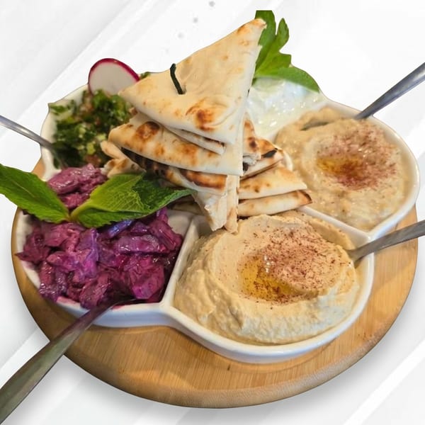 A white platter on a wooden board with hummus, red cabbage salad, tabbouleh, and pita bread.